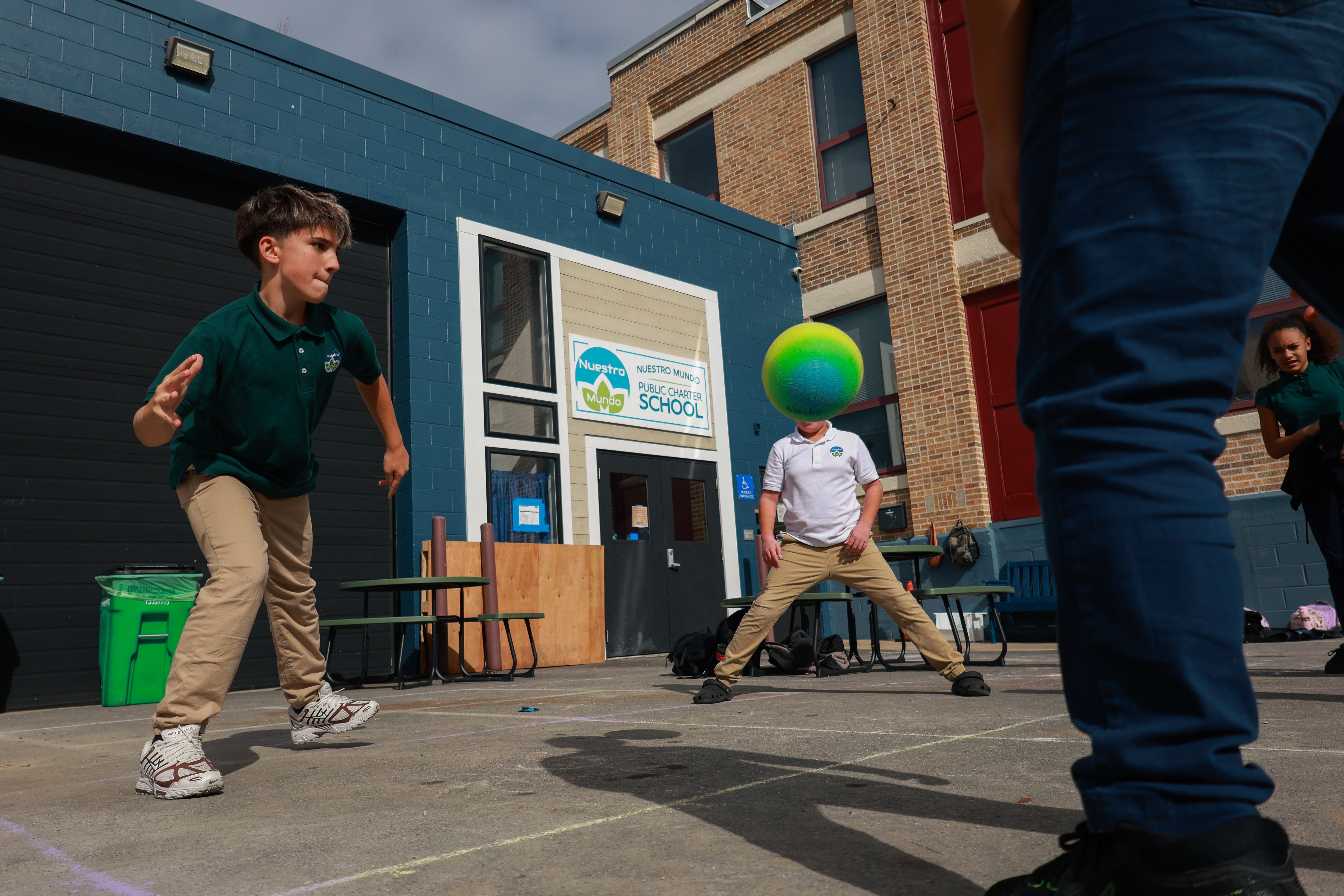 Photo of Beckham Gibb playing four square, with a blue and green ball obscuring another student's face.